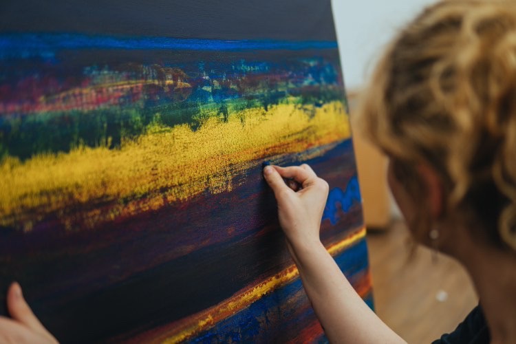 An artist adding detail to a large abstract landscape painting in their studio